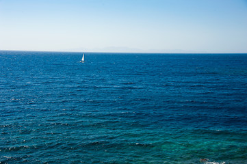 A lonely windsurfer, sailing in the endless blue ocean under the light blue sky of the Greek island Santorini / Thira 
