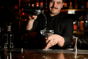 Bartender pours an alcohol from shaker to glass
