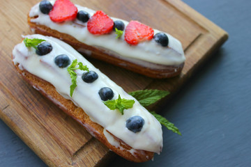 Delicious eclairs with strawberries and blueberries on a wooden cutting Board. Copy space. Beautiful and delicious dessert.