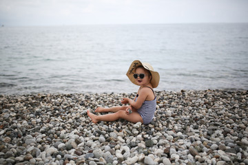 funny child sunbathes on beach in large straw hat
