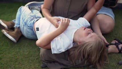 8-years old caucasian boy is laying on his mother knees playing with stones