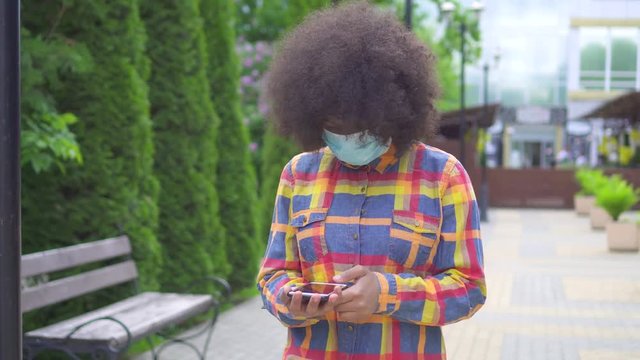 Portrait black american woman with an afro hairstyle in a protective medical mask with a smartphone in his hand