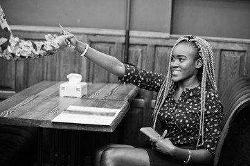 Portrait of beautiful young african business woman, wear on blue blouse and skirt, sitting at restaurant and gives credit card to waiter afro girl.