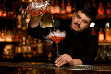 Bartender with strainer prepares an alcohol cocktail