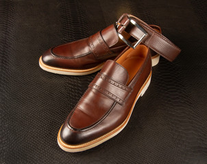 Men's shoes and brown belt against the background of python skin