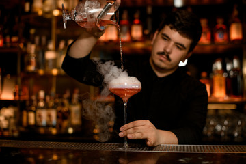 Bartender uses strainer to prepare an alcohol cocktail
