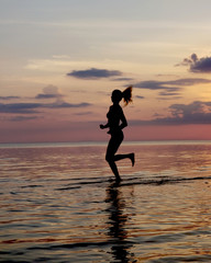 Fototapeta na wymiar silhouette of a girl run on the beach sand. Shooting against the sun. Sunset over the sea