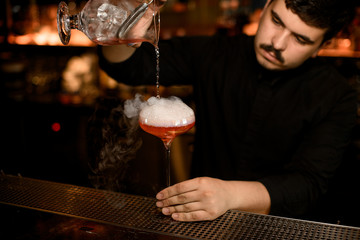 Bartender uses strainer to pour an alcohol drink