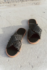 black wicker shoes with flat sole. Stylish summer slates without legs. Fashionable female slippers on gray asphalt with a shadow on it.