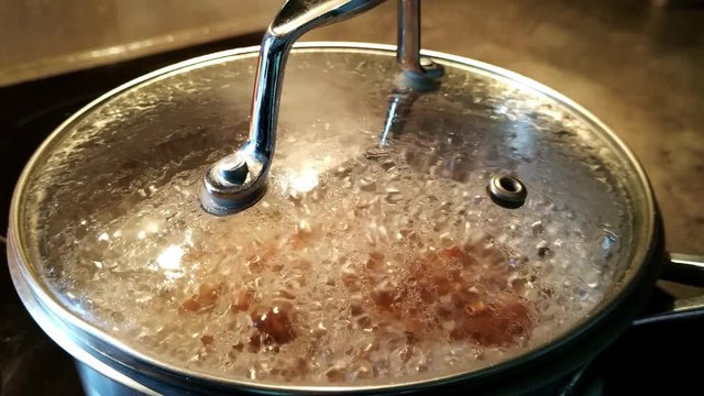 Buckwheat boiling in water in a saucepan with clear see-through lid on top