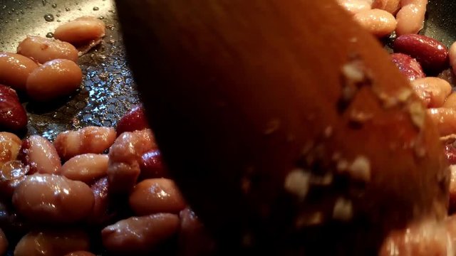 Close up of stirring and cooking red kidney beans in a black pan