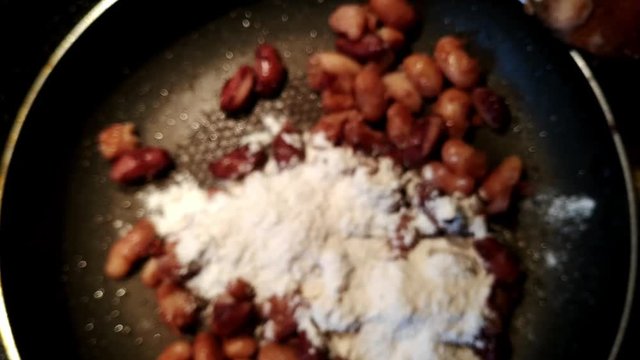 Adding flour to red kidney beans in a pan and mixing with a wooden spoon