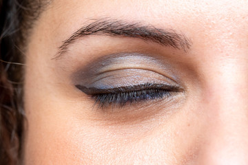 A closeup view on the closed eye of a young Caucasian woman, showing a dark blue shade of eye shadow makeup on upper lid, black mascara on the lashes and dark eyeliner on the lower lid.