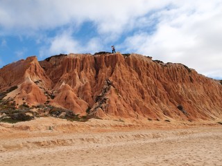 Fototapeta na wymiar Red high cliffs at Praia da Falesia, a paradise beach in Albufeira in Portugal with a couple kissing