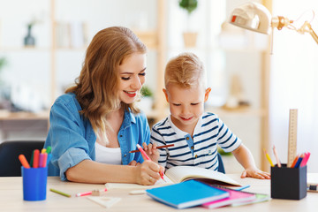 mother and child son doing homework writing and reading at home.