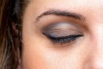 A close up view on the eye of a pretty Caucasian lady, with eyelid closed, showing a blue color eye shadow with dark mascara on the eyelashes and black penciled eye-liner.