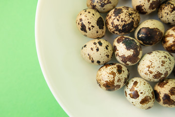 Obraz premium Raw quail eggs in white plate on green background. Easter.