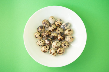 Raw quail eggs in white plate on green background. Easter.