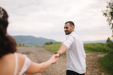 Handsome man leads his bride to beautiful Carpathian mountains. Happy wedding couple