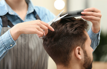 Barber making stylish haircut with professional scissors in beauty salon, closeup