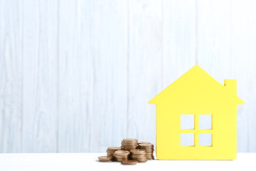 House model and coins on table against wooden background. Space for text