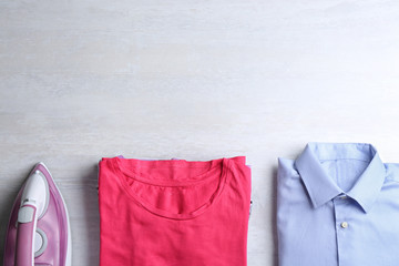 Flat lay composition with folded clothes and modern iron on light table. Space for text