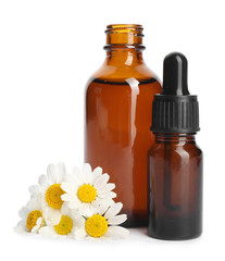 Chamomile flowers and cosmetic bottles of essential oil on white background