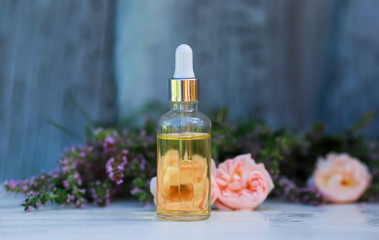 bottle with cosmetic rose oil and a pipette stands on a wooden table in delicate lavender colors outside