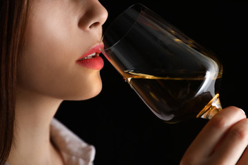 Young woman with glass of luxury white wine on black background, closeup view