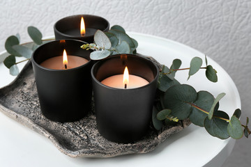 Tray with burning candles and branches on table