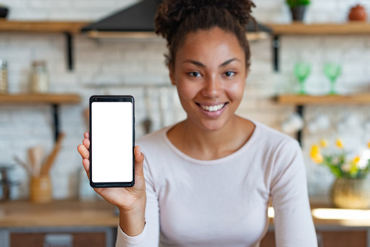 Young smiling woman sits and showing a mockup with white screen of cell telephone . - Image