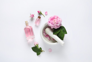 Composition with rose essential oil and flowers on white background, top view