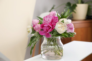 Vase with bouquet of beautiful peonies on table in room