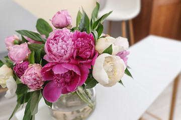 Vase with bouquet of beautiful peonies on table in room, space for text