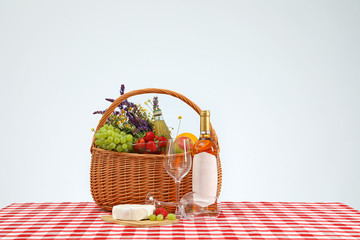 Picnic basket with wine and products on checkered tablecloth against white background