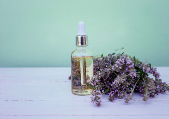  glass bottle with cosmetic oil stands on a wooden white table in delicate lilac flowers  thyme