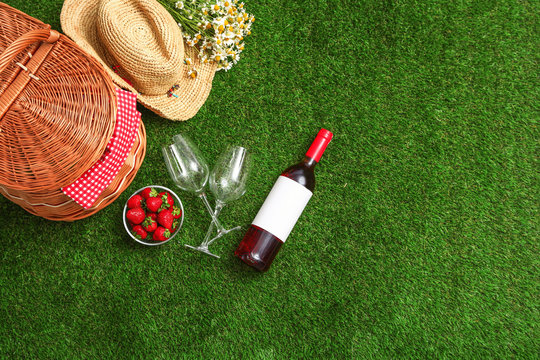 Flat lay composition with picnic basket, wine and strawberries on grass, space for text
