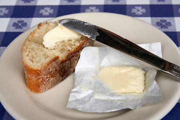 piece of crusty bread spread with butter from a wrapped pat sitting on a plate with a knife on a...