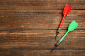 Dart arrows on wooden background, flat lay. Space for text