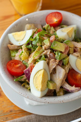 Traditional american cobb salad with chopped avocado, tomatoes, hard boiled egg, roasted chicken and greens for a healthy lunch, served on wooden table with soft light