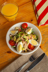 Top view of traditional american cobb salad with chopped avocado, tomatoes, hard boiled egg, roasted chicken and greens for a healthy lunch, served on wooden table with soft light