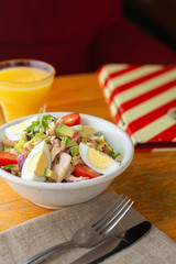 Traditional american cobb salad with chopped avocado, tomatoes, hard boiled egg, roasted chicken and greens for a healthy lunch, served with orange juice