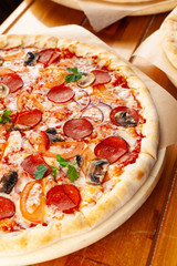 Close up of half pizza on thin dough with spicy chorizo, cheese, champignons, tomatoes, ricotta and red onion, served on rustic wooden table