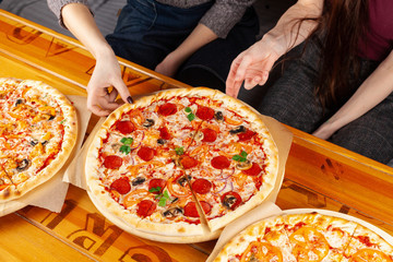 People eating pizza on thin dough with spicy chorizo, cheese, champignons, ricotta and red onion, holding pieces in hands