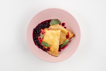 Traditional russian crepes blini with sweet blueberry sauce, folded, served on bright dishware and isolated on white