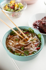 Close up side view of hot traditional pho bo with noodles, beansprouts, chili pepper and beef with other meals on background