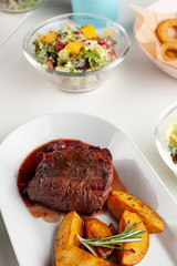 Juicy grilled veal steak with berry sauce and seasoned roasted potato wedges with meals on background
