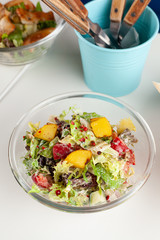 Close up of nutritious rustic-style salad with mixed greens, vegetables, roasted potato wedges and red onion, served with other meals on a background