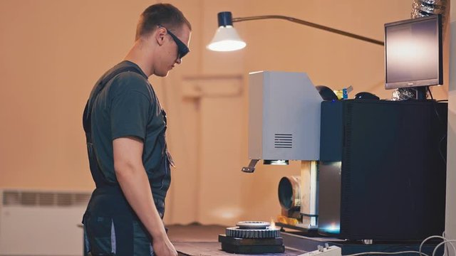 Worker makes laser engraving on a metal part. Laser machine makes engraving