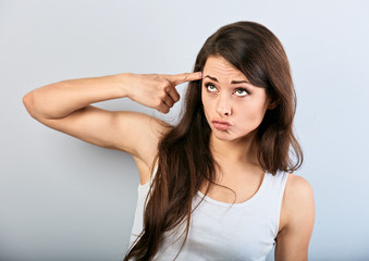 Fototapeta premium Young beauiful girl showing finger gun gesture, shooting herself and looking up on blue background.